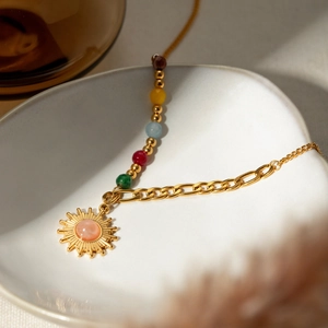Macro detail of 18k gold sun pendant with pink gemstone and colorful beads on tray