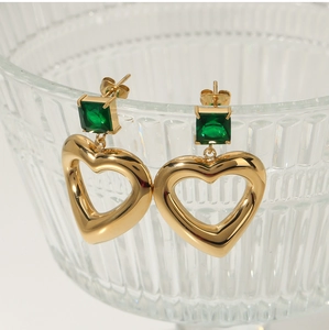 Macro shot of gold-plated stainless steel earrings with green square zircon and heart charm