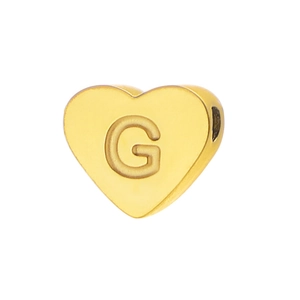 Macro view of gold heart-shaped bead with embossed letter G for DIY jewelry making