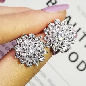 Detailed close-up showing a flower-shaped zircon stud earring held by fingers