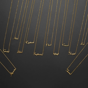 Set of 12 zodiac script gold necklaces with letter pendants on black background