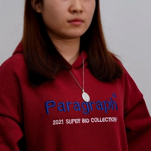 Detail of red hoodie with blue embroidered Paragraph 2021 text and silver necklace