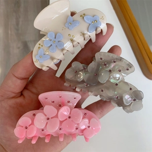 Close-up of three acetate flower hair claws with rhinestones in beige, grey, and pink