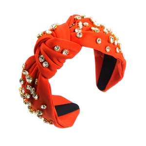 Close-up of orange knotted headband with sparkling rhinestones in gold metal settings