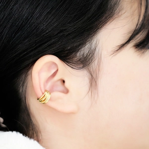 Macro shot of layered gold ear cuff showing polished multi-line texture on the ear