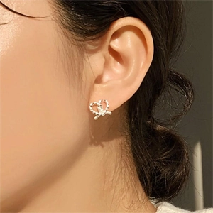 Close-up of minimalist silver heart-shaped twisted knot stud earring worn by a model