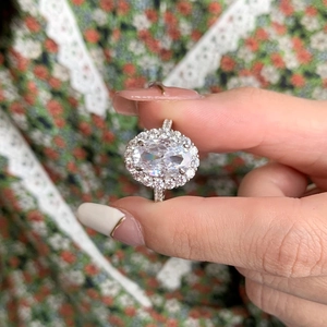 Detailed close-up of a halo set oval-cut silver ring with sparkling clear gemstones