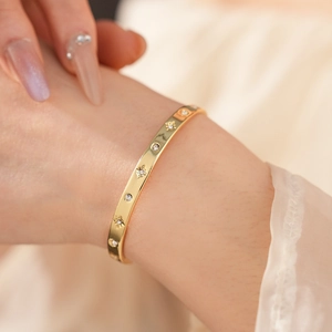 Détail d'un bracelet doré avec oxydes de zirconium et motifs étoiles gravés au poignet