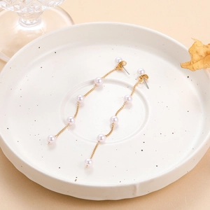 Close-up of gold chain pearl heart tassel earrings on a decorative ceramic tray
