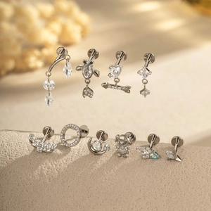 Titanium G23 cartilage earrings set featuring gold and zircon shapes on a sandy background