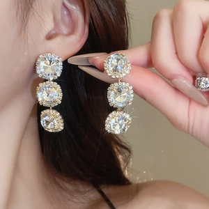 Close-up of gold stud earrings with three round diamonds worn by a female model