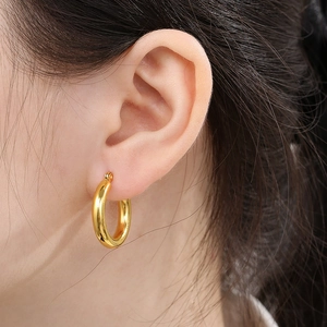 Close-up of golden chunky hoop earrings with a polished mirror finish on a female model