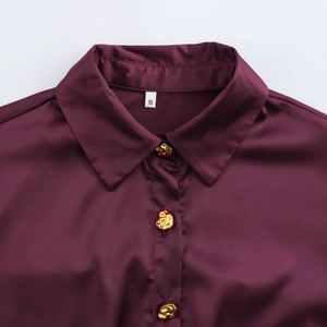 Detail of wine red satin blouse featuring lapel collar and golden metallic buttons