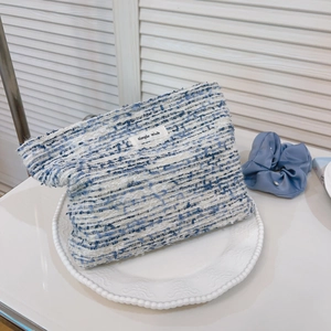 Detail of blue tweed cosmetic bag with woven texture and white fabric label on a ceramic tray