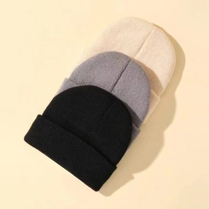 Detailed close-up of three knitted beanies in black, dark grey, and warm beige colors