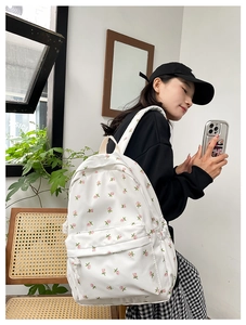 Close-up of a white floral backpack shown from the side on a model in a natural setting
