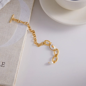 Détail du bracelet chaîne dorée avec fermoir OT, breloque florale et perle blanche