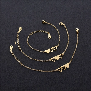 Close-up of three gold heart charms bracelets with lobster clasp on grey texture