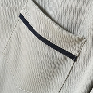 Macro shot of men's polo shirt with light gray piqué texture and navy pocket trim