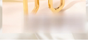 Macro shot of gold U-shaped hoop earrings on elegant beige silk fabric background