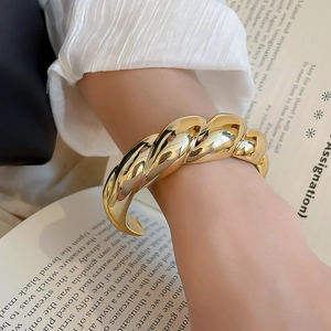 Detailed view of a gold-plated twisted acrylic bangle with a polished mirror finish