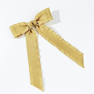 Close-up of golden satin bow hair clip with elegant ruffled edges and long flowing ribbons