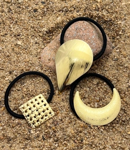 Close-up of golden teardrop and crescent metal hair ties on beach sand background