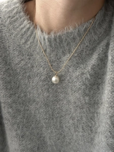 Detail of elegant white pearl pendant on a gold snake chain worn on a grey sweater