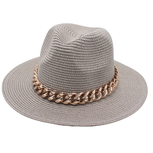 Détail d'un chapeau fedora en paille grise avec une grosse chaîne en métal doré