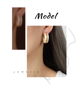 Close-up of C-shaped gold-plated earrings with white enamel and embossed texture on model