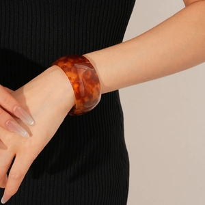 Detail of tortoiseshell wide acetate open bangle showing amber texture on female wrist