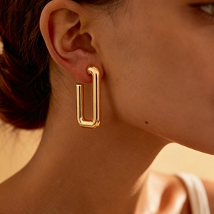 Close-up of a model wearing a glossy gold U-shaped rectangular geometric metal earring
