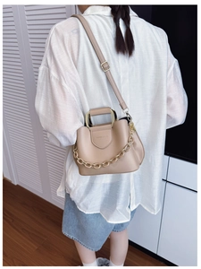 Detail of beige PU leather bucket bag featuring gold metal handle and decorative chain link