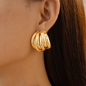Macro view of gold layered textured geometric hoop earrings on a model’s ear