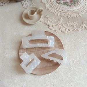 Three-piece set of pearlescent cream acetic hair claws in geometric shapes on a wooden tray
