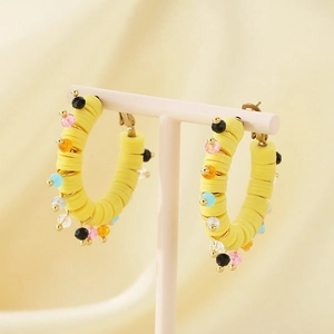 Détail de créoles jaunes avec perles colorées et tranches de résine sur fond de soie