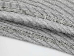 Makro-Detail von grauem Rippstoff mit Fokus auf die hochwertige Saumverarbeitung am Top