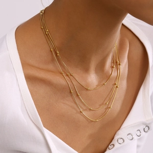 Detailed view of triple-layer gold bead necklace on model neck with layered design