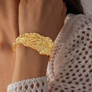 Close-up of golden chunky cuff bracelet featuring irregular lava texture and wrinkled metal