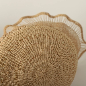 Detail of natural raffia sun hat with woven texture, wavy edges and gold thread accents