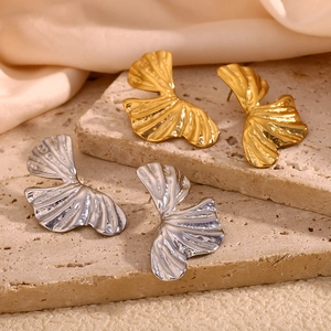 Detailed view of gold and silver ginkgo leaf earrings on textured stone and silk