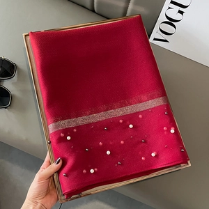 Close-up of red silk scarf featuring gold glitter trim and decorative pearl embellishments