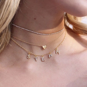 Close-up of layered gold tone necklaces featuring rhinestone choker and heart S pendant
