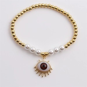 Macro detail of gold beaded bracelet with white pearls and red evil eye charm