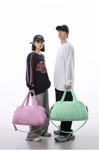 Two models holding large pink and mint green travel duffel bags in a studio setting