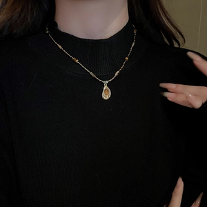Détail d'une chaîne dorée avec pendentif œil de tigre en goutte sur un pull noir chic
