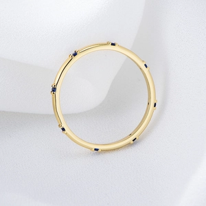 Minimalist gold band ring with blue cubic zirconia stones on white textured fabric