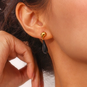 Close-up of a model wearing a gold and black teardrop earring with smooth metallic finish