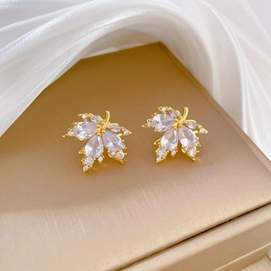 Macro detail of gold maple leaf earrings with cubic zirconia on a silk display