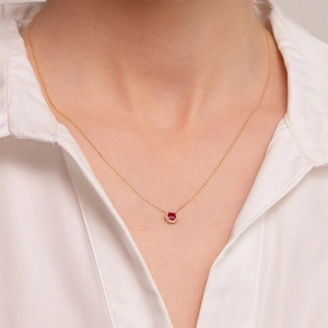 Close-up of a halo ruby pendant necklace with gold chain worn on a white shirt